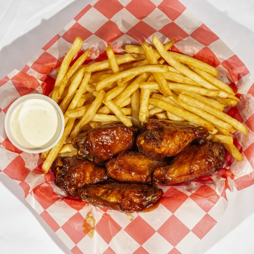 Bear's Den Pizzeria's BBQ wings and golden french fries in a red and white checkered basket.