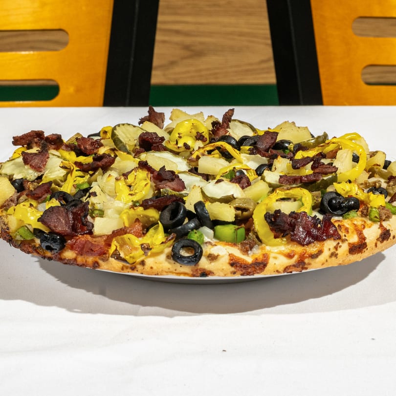 Bear's Den Pizzeria's pizza, loaded with bacon, black olives, banana peppers, and pickles.