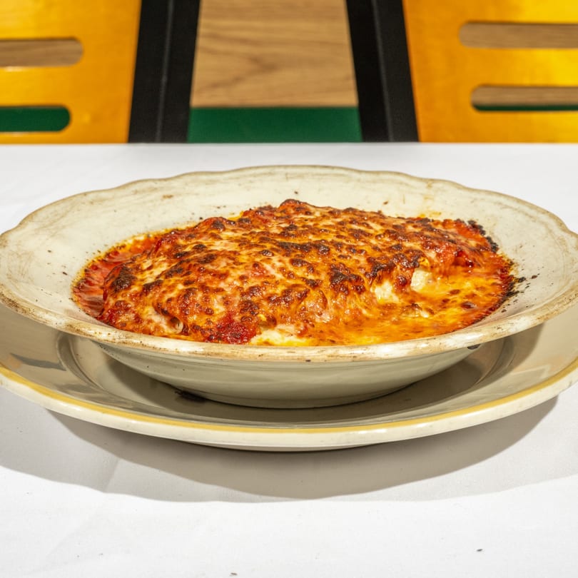 A baked dish of lasagna with melted, bubbly cheese and red sauce in a rustic bowl.